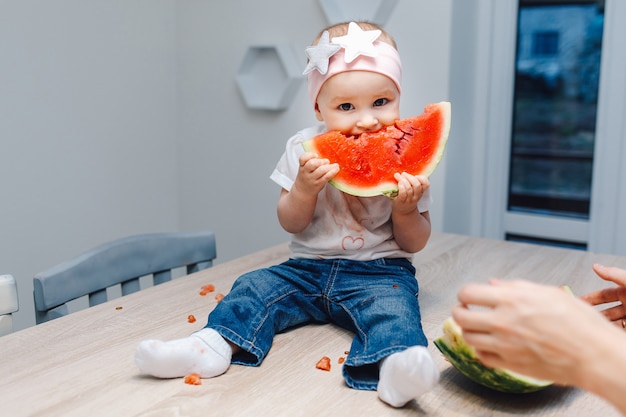 Bebé bonito que come a melancia na cozinha