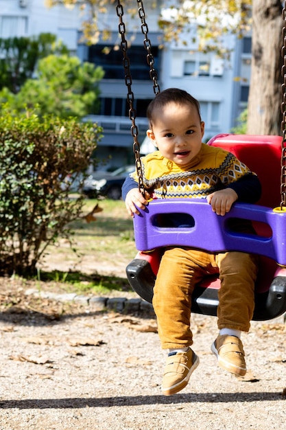 Foto bebê bonito se divertindo no playground ao ar livre atividades de bebê feliz balançando no balanço