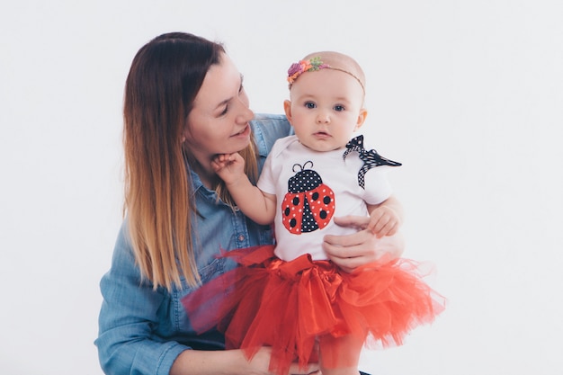 Bebé en los brazos de la madre. Sobre fondo blanco Mujer con un niño. Moda para niña.