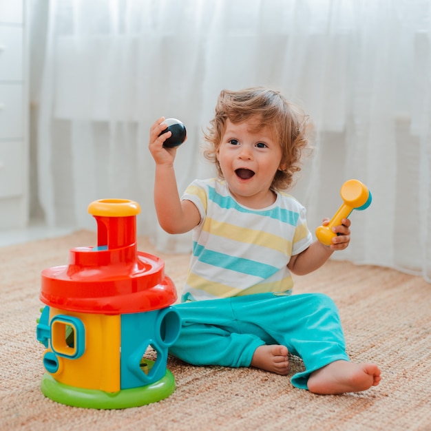 Bebê brinca no chão da sala em brinquedos plásticos educativos.