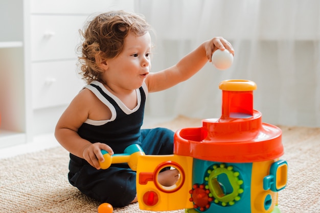 Bebê brinca no chão da sala em brinquedos plásticos educativos.