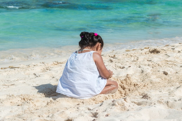 Bebê brincando na areia perto do mar. uma menina sentada na praia. silhueta de menina com o mar ao fundo. construindo castelo de areia