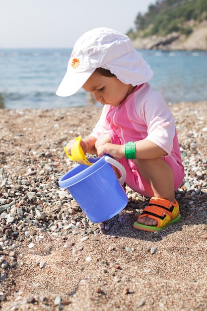 Bebê brincando na praia com rebbles e balde