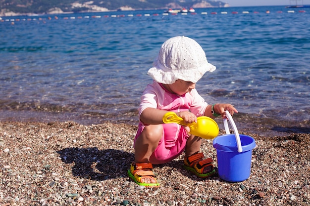 Bebê brincando na praia com rebbles e balde