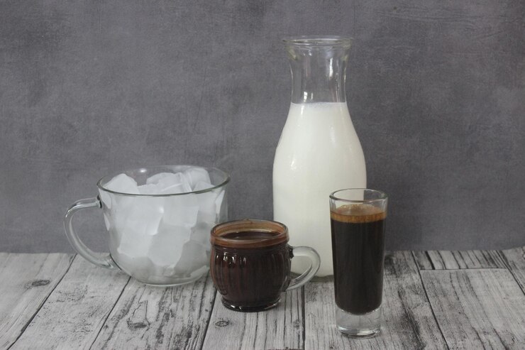 Foto bebe café e leite com chocolate mochacino em copo e garrafa em mesa de madeira contra a parede cinzenta
