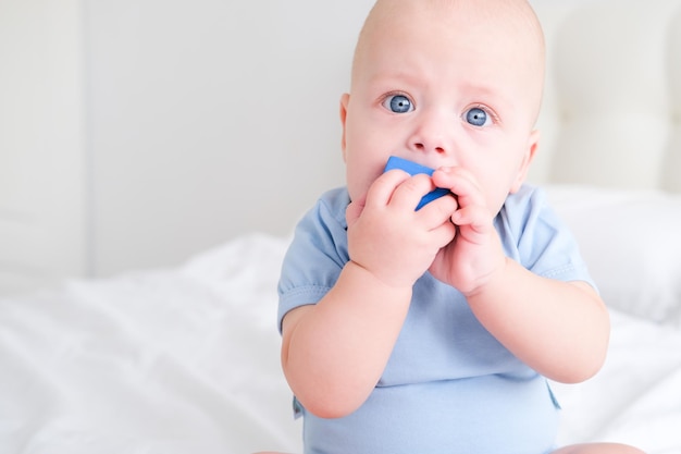 Bebé calvo de 3 meses con traje azul jugando con juguetes de cubos de madera para niños en la cama