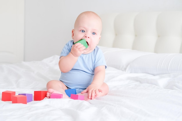 Bebé calvo de 3 meses con traje azul jugando con juguetes de cubos de madera para niños en la cama