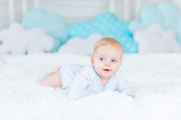 Bebé en la cama con pijama azul se acuesta o se despierta por la mañana bebé rubio seis meses