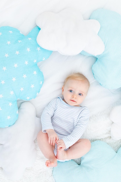 Bebé en la cama con pijama azul se acuesta o se despierta por la mañana bebé rubio seis meses