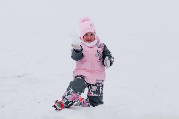 Bebé a caminar en invierno niña en cálido traje de esquí y motos de nieve con botas jugar en la nieve