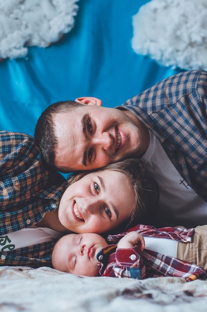 Foto bebé en una camisa a cuadros con papá y mamá. bebé y sus padres. foto de familia. apoyarse en las mejillas del otro