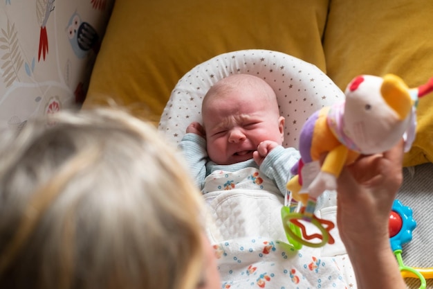 Bebé caucásico de dos meses en la cama mirando un juguete de puf llorando. Emoción infantil negativa