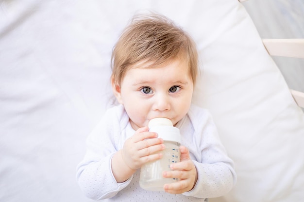 bebé chupando una botella de leche en una cama de algodón blanco en casa niña bebé linda comiendo leche concepto de comida para bebés retrato en primer plano