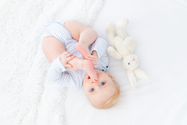 Bebé chupando el pie acostado en la cama, bebé rubio de seis meses