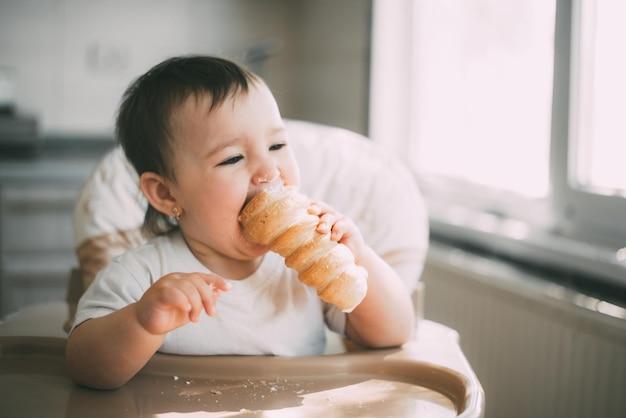 El bebé en la cocina come con avidez deliciosos tubos cremosos rellenos de crema de vainilla