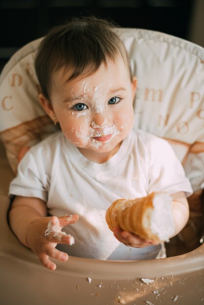 Bebé en la cocina comiendo ansiosamente los deliciosos cuernos de crema, rellenos con crema de vainilla