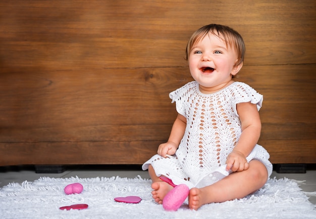 Bebê com corações em um fundo de madeira. bebê sentado no tapete com corações rosa rindo no fundo de madeira