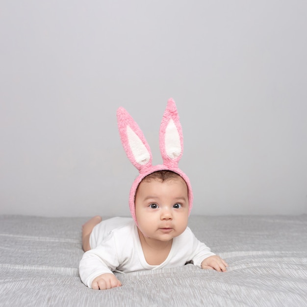 Bebê com orelhas de coelho está em uma cama de luz cinza O conceito de uma Maquete de Páscoa Feliz para cartões postais de celebração de design de publicidade Copiar espaço