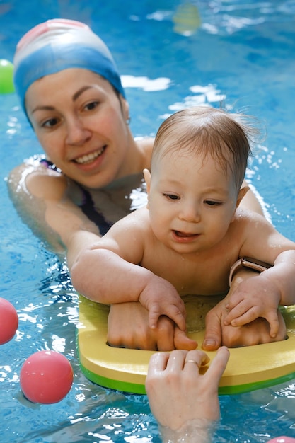 Bebê com treinador de mãe na piscina coberta tendo aula