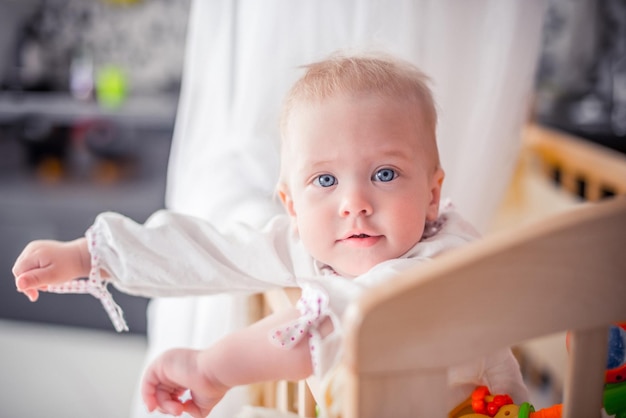 Foto bebê com um lindo rosto feliz está de pé em um berço e sorrindo, crianças engraçadas, família feliz