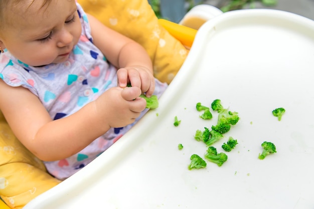 El bebé come trozos de verduras con brócoli. Enfoque selectivo. Niño.