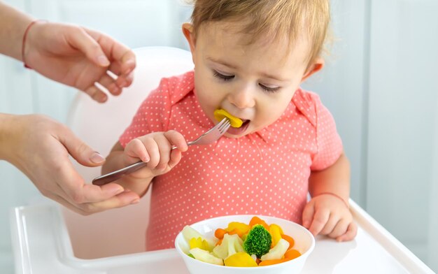 El bebé come verduras en una silla Enfoque selectivo Niño