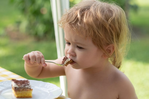 Bebê comendo bolo menino fofo come doces o menino loiro está comendo bolo lá fora criança com fome