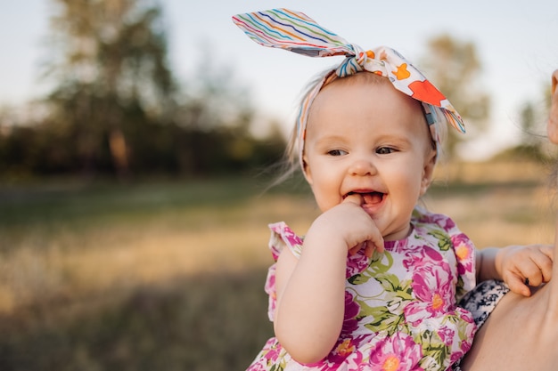 Bebé complicado en las manos. Niño astuto en pastizales. Niña pequeña en las manos abrazando. Moda infantil con sombreros