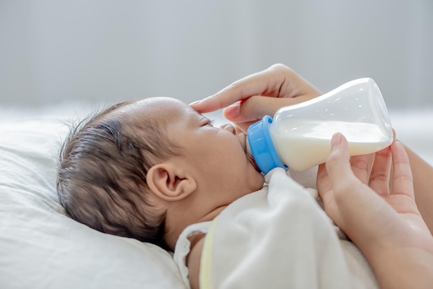 Bebê consome leite de mamadeira alimentado pela mãe e toca seu filho com ternura