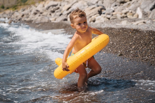 El bebé corre hacia el mar en un círculo inflable amarillo El niño se prepara para nadar Está feliz y riendo