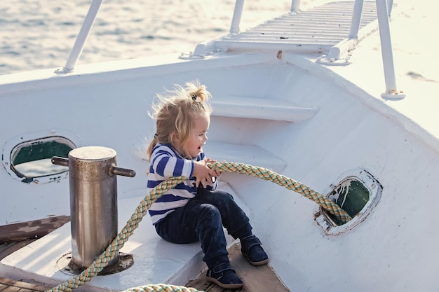 Bebê criança brincando com corda no iate Criança sentada e ancorando a corda no barco branco Viagens e férias de verão Cuidados com o bebê e infância Conceito de iatismo e vela