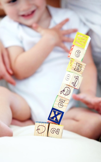 Foto bebê criança e brincar com blocos para aprender sorriso e feliz em casa creche na cama criança pequena madeira e criança com brinquedos para a educação alfabeto e desenvolvimento de menino bonito com números closeup