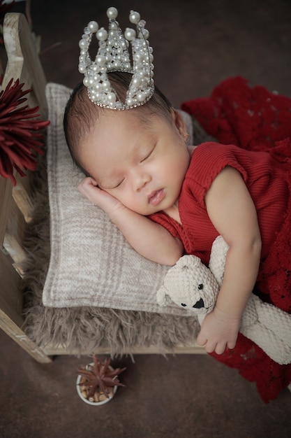 Bebé cubierto de ropa roja con corona en la cabeza durmiendo en una almohada blanca