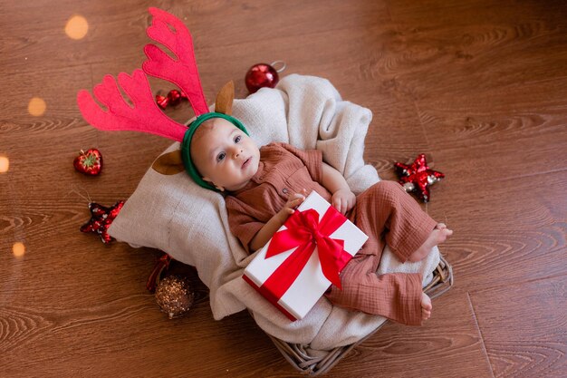 Bebé con cuernos de ciervo en la cabeza yace sobre una manta de lino gris en una cesta de mimbre. Navidad, año nuevo. Regalo de Navidad. El pequeño ayudante de Papá Noel. espacio para texto. foto de alta calidad