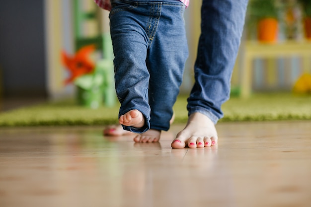 Foto bebê dando os primeiros passos com a ajuda da mãe em casa. conceito de família feliz