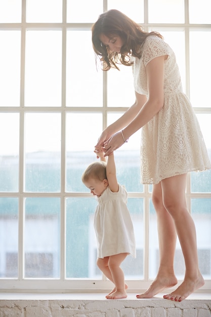 Bebé dando los primeros pasos con la ayuda de la madre en casa. Bebé inclinado caminando con madre