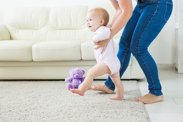 Bebé dando los primeros pasos con la ayuda de la madre en casa