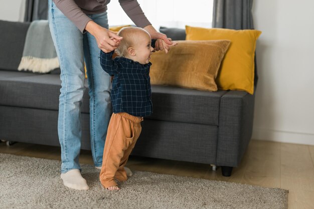 Bebé dando los primeros pasos con la ayuda de la madre en casa