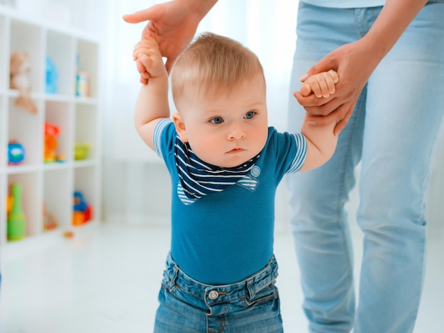 Bebé dando los primeros pasos con la ayuda de la madre en casa