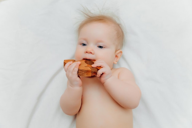 Bebê de 6 meses segura em suas mãos um brinquedo de dentição de madeira deitado em um berço em um quarto infantil