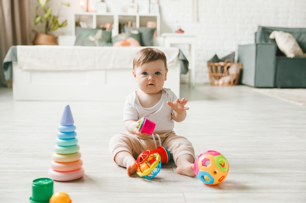Foto bebê de 69 meses brincando com uma pirâmide colorida de arco-íris sentado em um quarto branco e ensolarado brinquedos para crianças pequenas interior infantil uma criança com um brinquedo educativo