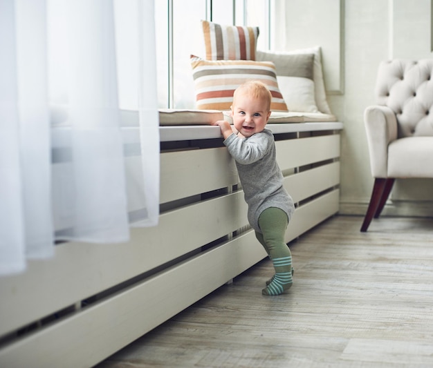 Bebê de 8 meses fica com suporte perto da janela em casa no quarto branco