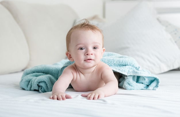 Bebê de 9 meses na toalha azul após o banho rastejando na cama