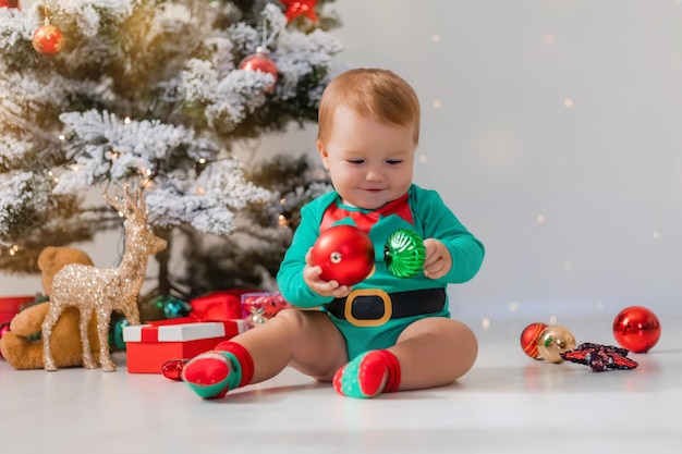 bebê de macacão verde segura bolas de natal coloridas em suas mãos criança em uma fantasia de gnomo de natal