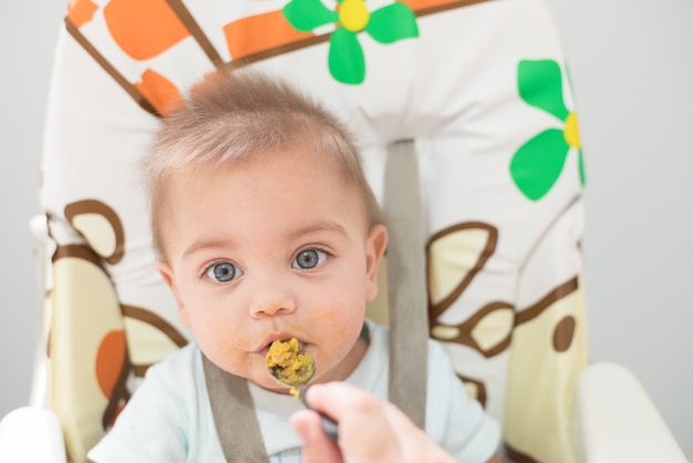 Bebé de olhos azuis que come na cadeira do bebê