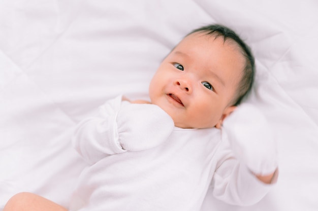 Bebê de sorriso que encontra-se em uma cama branca, manhã da família em casa, higiene das crianças.