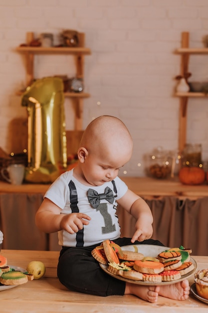 Bebê de um ano come pão de gengibre pintado em casa. primeiro aniversário em uma atmosfera festiva. lanche saudável para crianças. menino está sentado à mesa da cozinha. Foto de alta qualidade