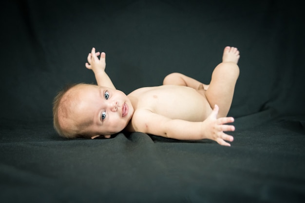 Foto bebé desnudo eyed azul que miente en tela negra