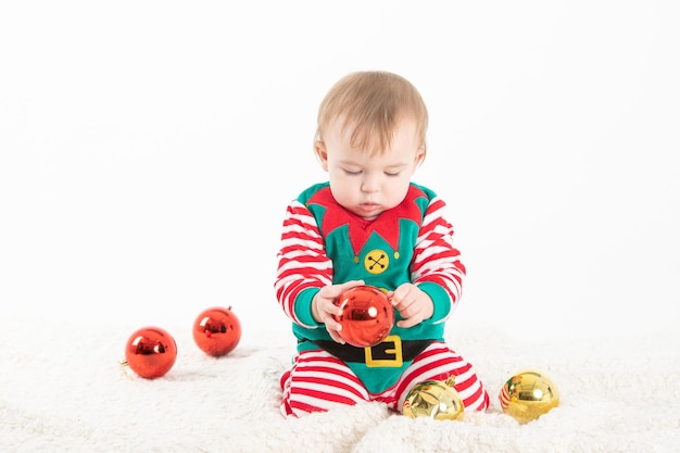 Bebé disfrazado de elfo agarrando bolas de navidad con expresión seria