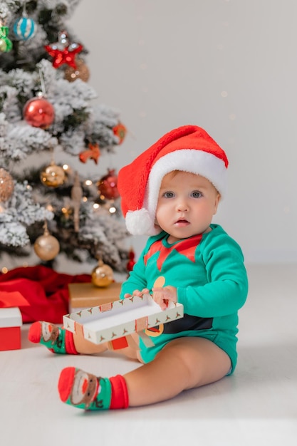 bebé disfrazado de gnomo de Navidad abre regalos cerca de productos de árboles de Navidad para niños y vacaciones